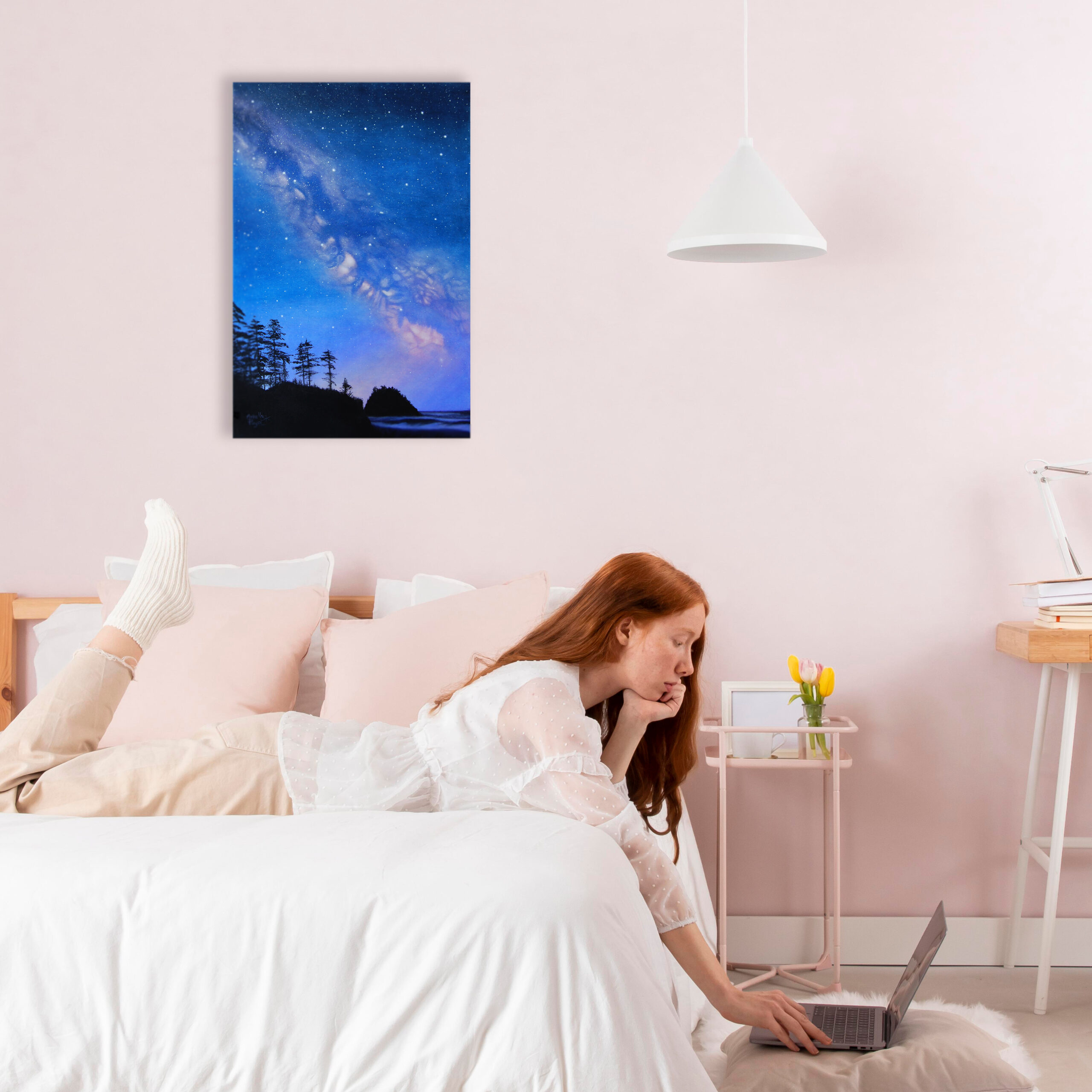 Peinture à l'acrylique intitulée "Pluie d'étoiles" par Arielle Payet montrant la voie lactée au dessus d'un paysage côtier mis en situation dans une chambre avec une jeune femme sur son ordinateur